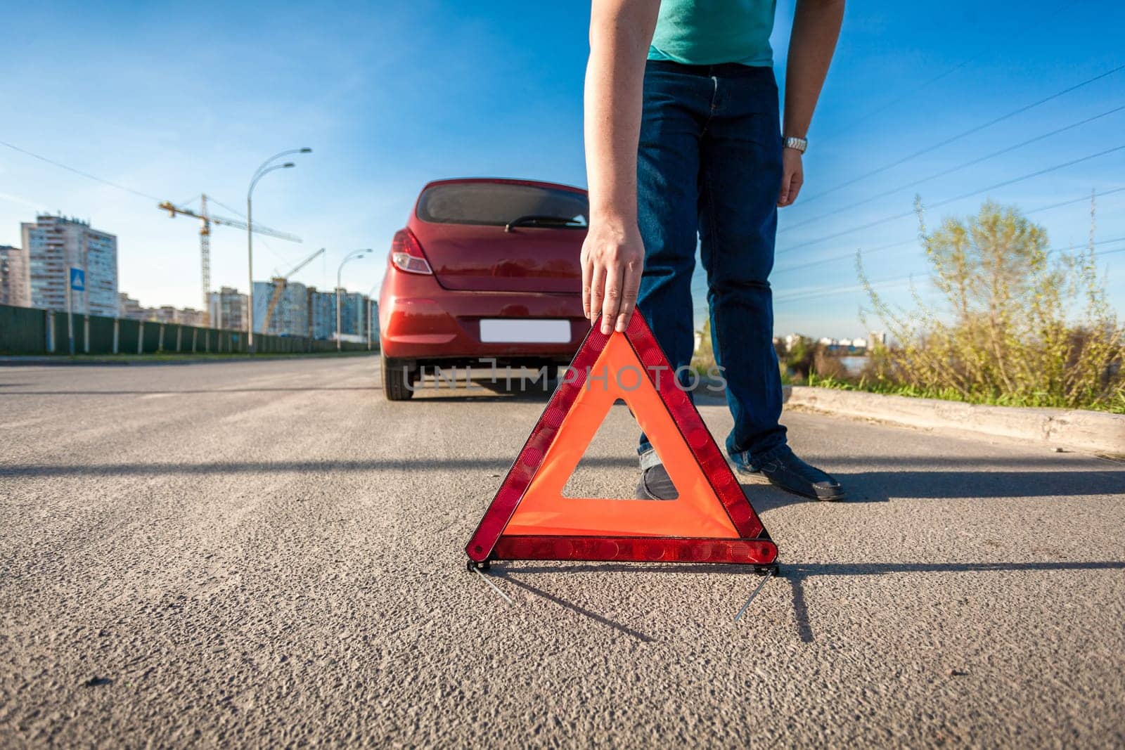 Young man placing red triangle sing on road after car crash