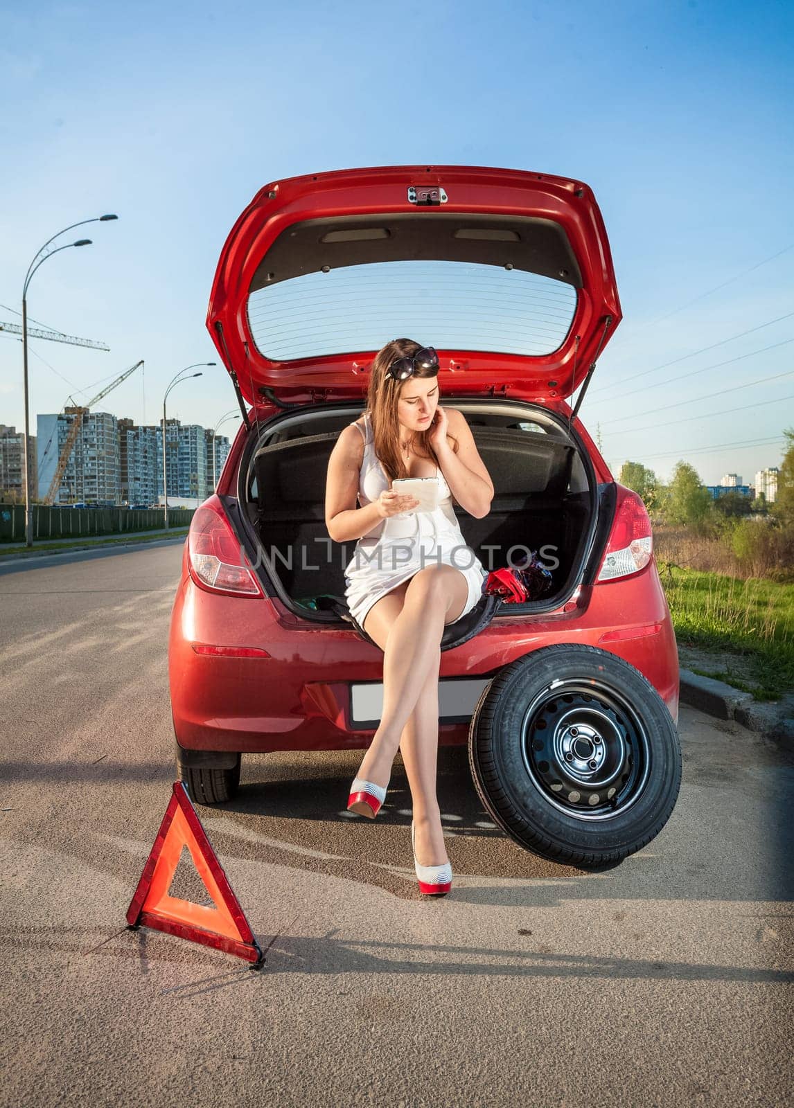 Sexy woman leaning against broken car and browsing hot to repair it on tablet