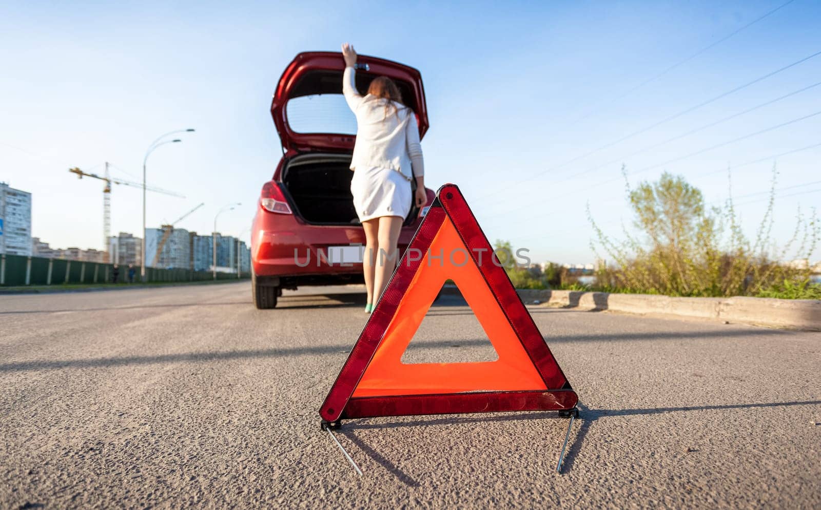 Photo of woman looking in trunk of broken car