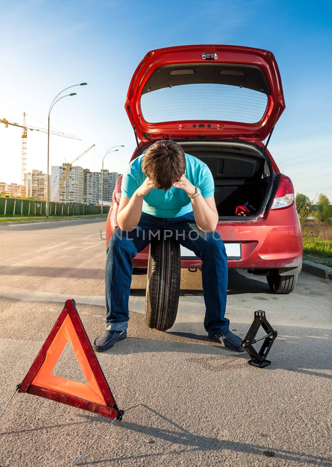 Portrait of sad man sitting on spare wheel near broken car