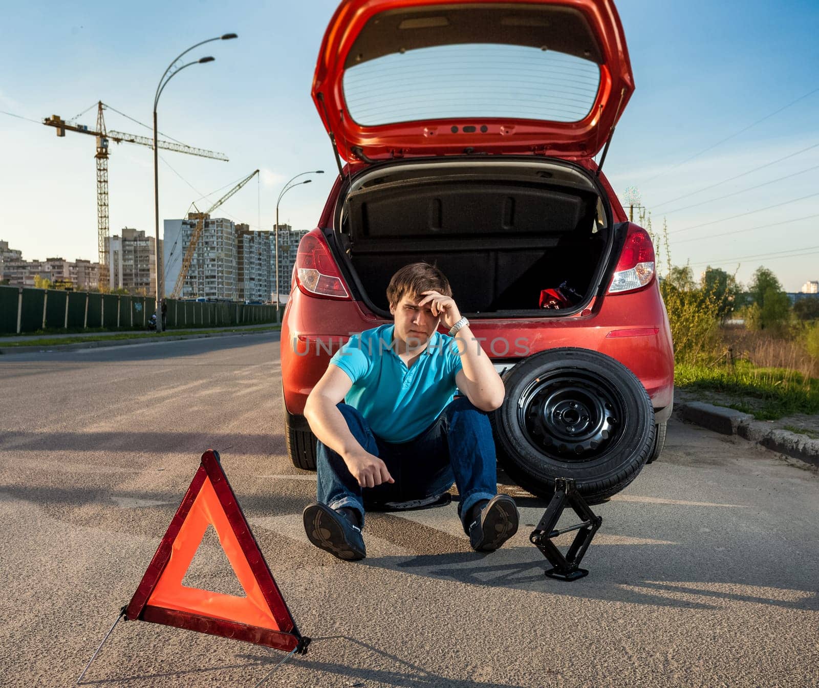 Sad and depressed man sitting near car with punctured tire