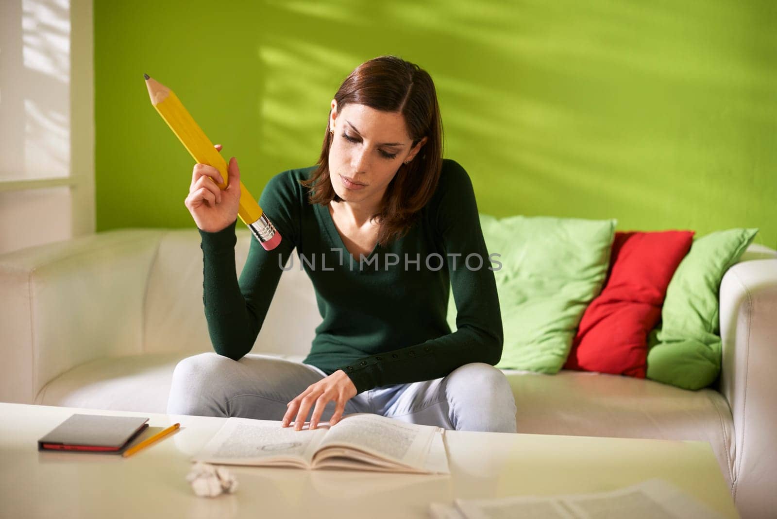 young caucasian student doing homeworks and taking notes on book with huge pencil at home
