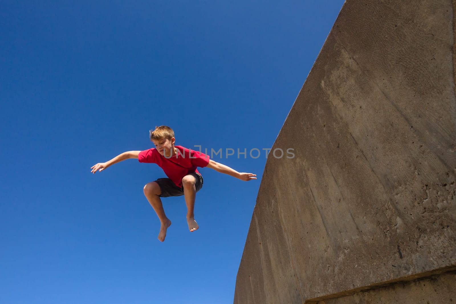 Teen boy jumping off wall in parkour off wall on beach