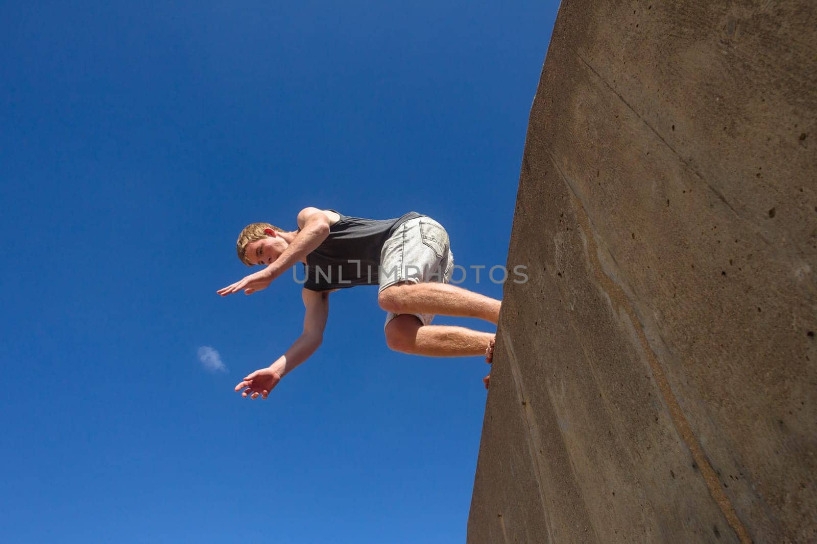 Teen boy jumping off wall into summersault flights off concrete wall parkour on beach