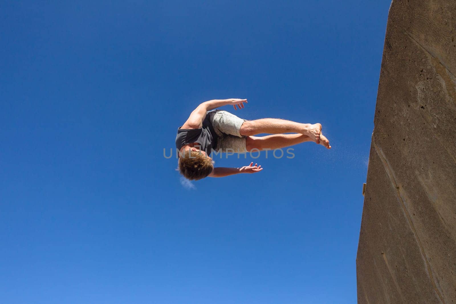 Teen boy jumping off wall into summersault flights off concrete wall parkour on beach