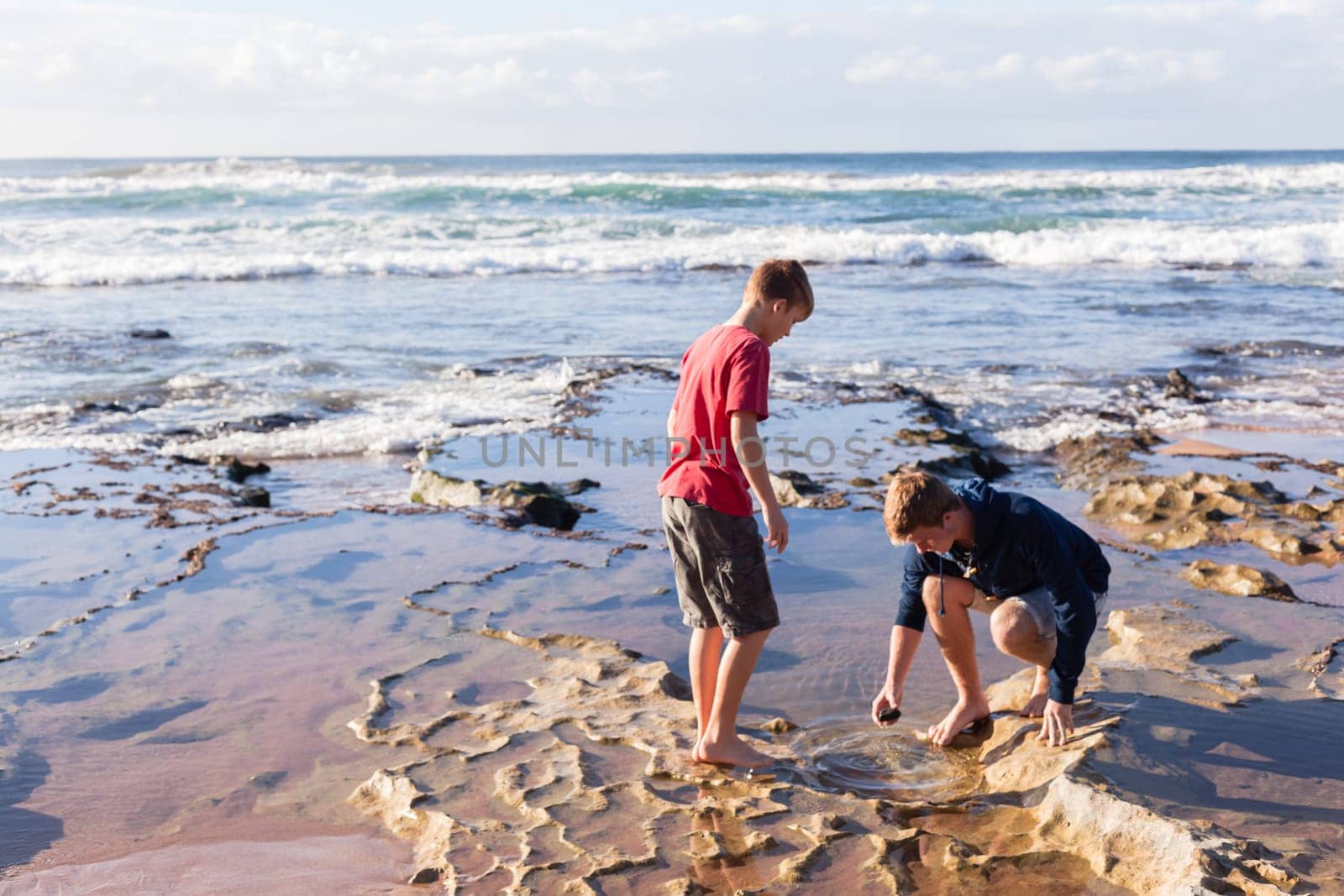 Teen boys family hangout together at the  beach ocean on clear blue day