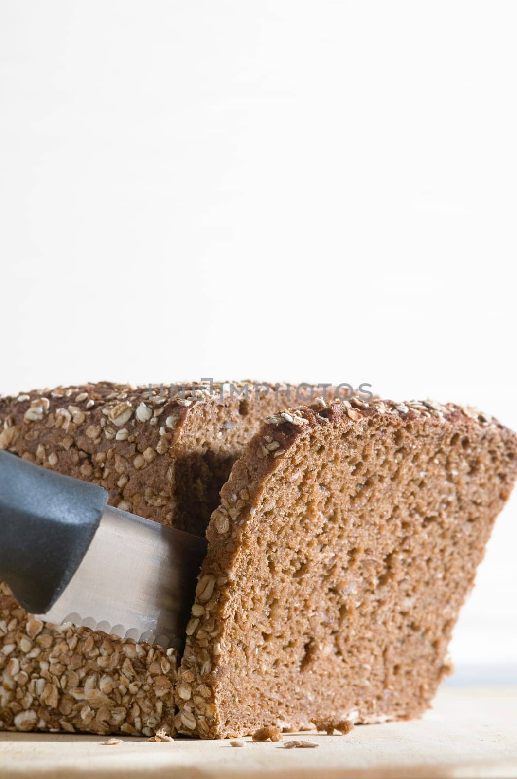 Still life with wholemeal bread and bread knife on cutting board against a bright background