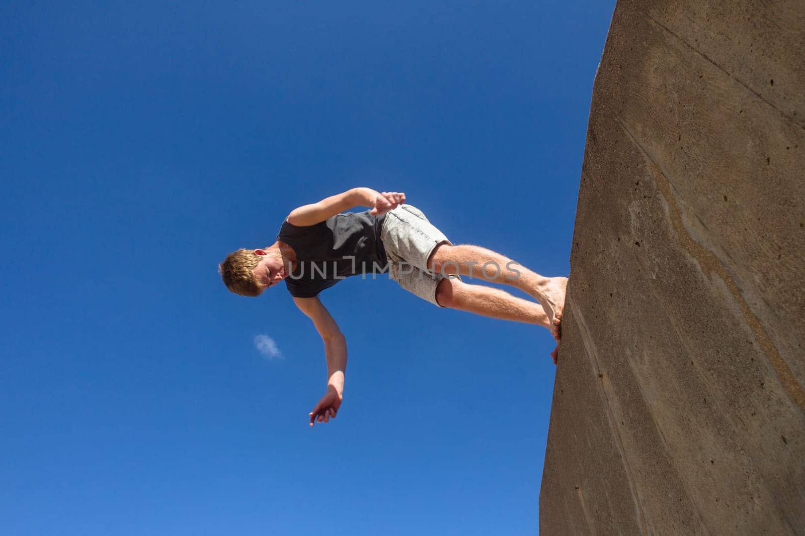 Teen boy jumping off wall into summersault flights off concrete wall parkour on beach