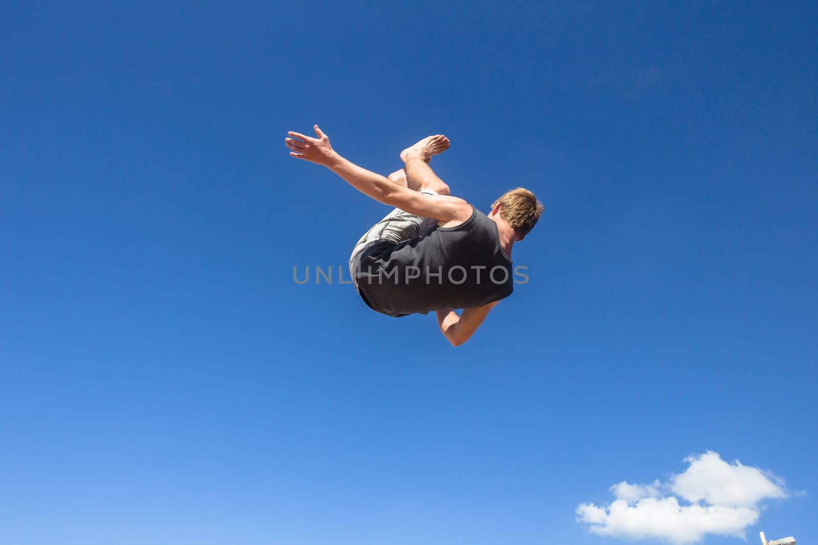 Teen boy jumping off wall into summersault flights off concrete wall parkour on beach