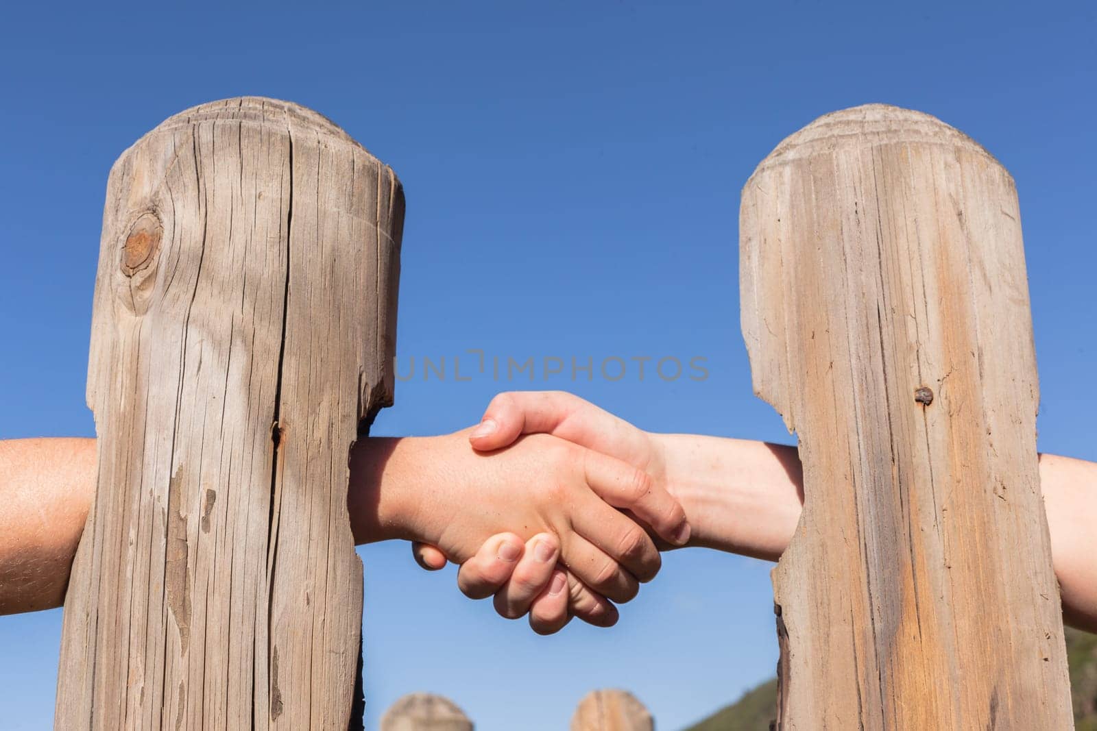 Close photo image of two hands through wood poles for a trust integrity distant handshake in persons business etc.