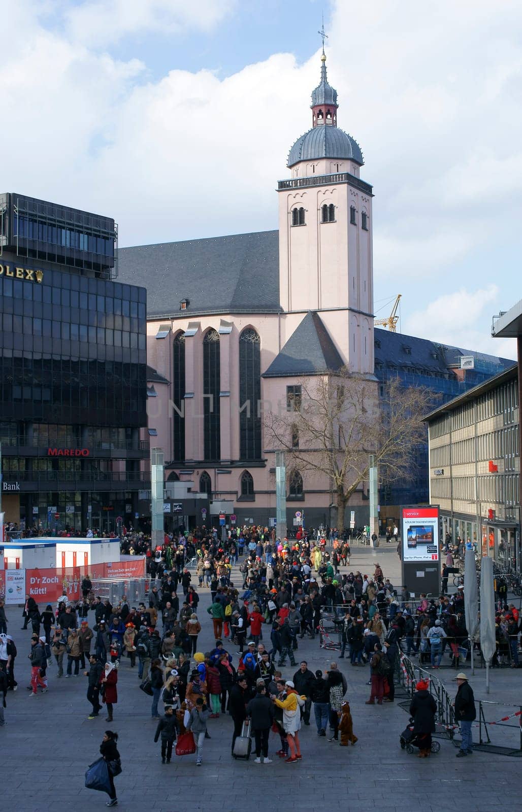 Cologne,Germany – March 02,2014: Colourfully dressed people walk to the carnival procession on the station forecourt in Cologne overlooking the St. Mary's Assumption Church on March 2,2014 in Cologne.