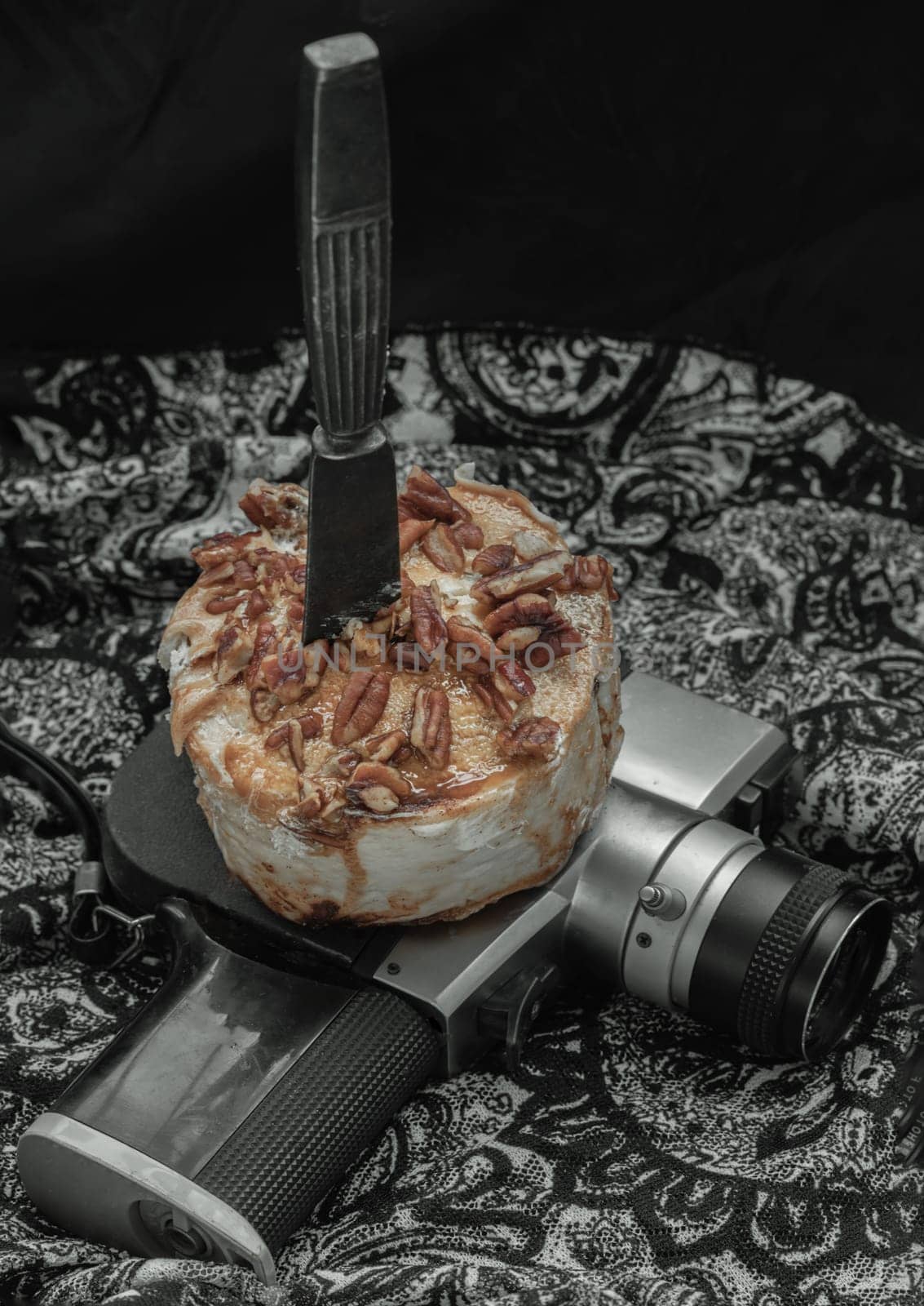 The black metal knife is inserted into the Caramel Pecan topped with caramel frosting and pecans on the old movie camera 8mm with dark background. Copy sapce, Selective focus.