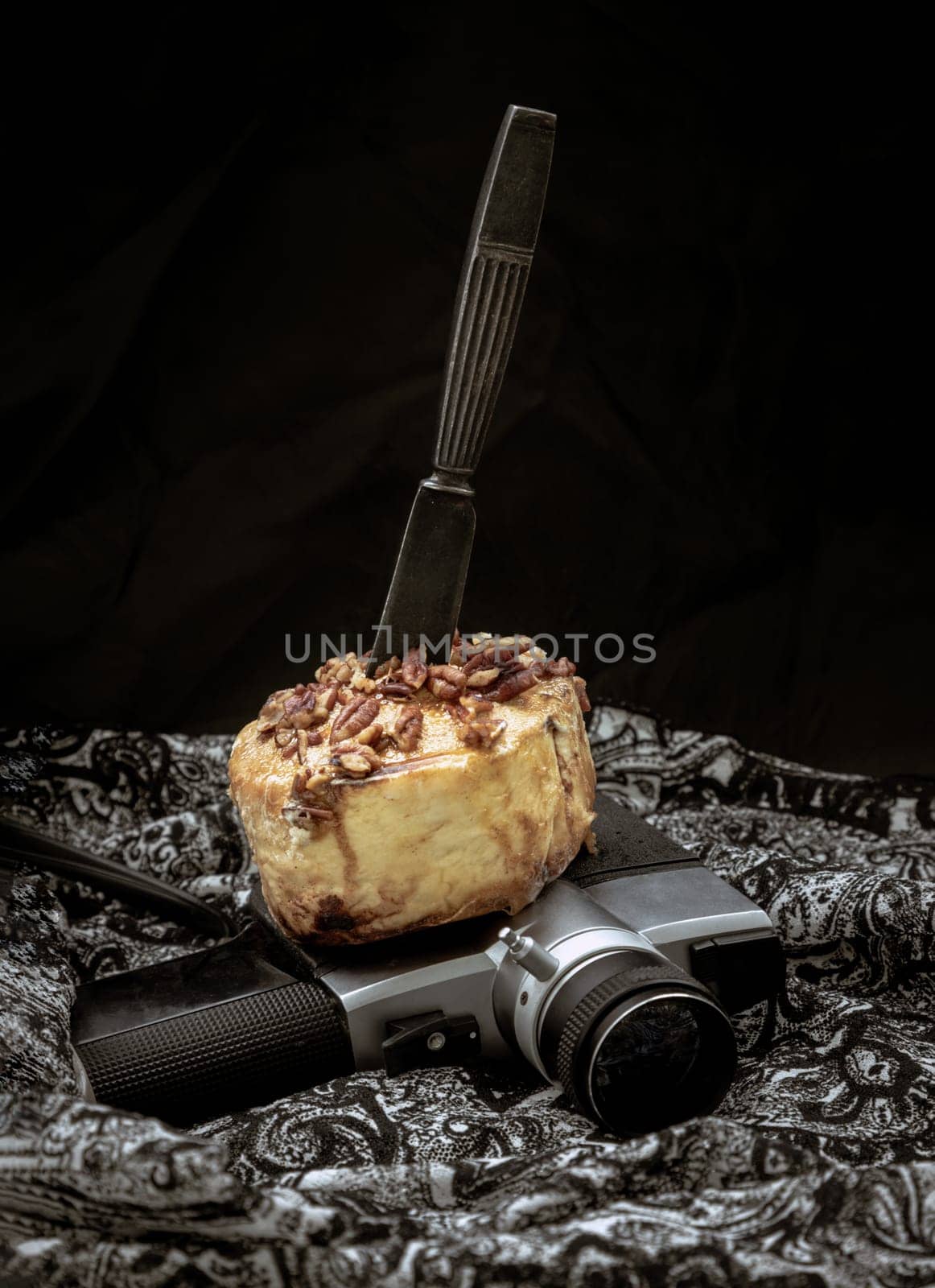The black metal knife is inserted into the Caramel Pecan topped with caramel frosting and pecans on the old movie camera 8mm with dark background. Copy sapce, Selective focus.