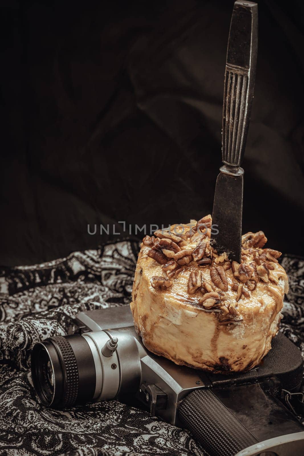 The black metal knife is inserted into the Caramel Pecan topped with caramel frosting and pecans on the old movie camera 8mm with dark background. Copy sapce, Selective focus.