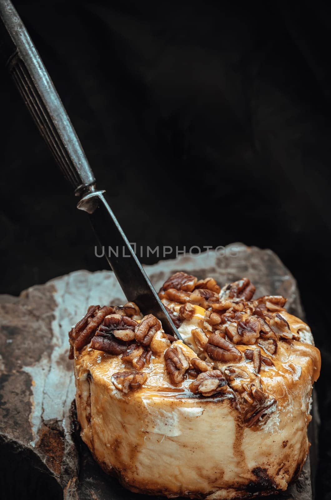 The black metal knife is inserted into the Caramel Pecan topped with caramel frosting and pecans on rock with dark background. Copy space, Selective focus.