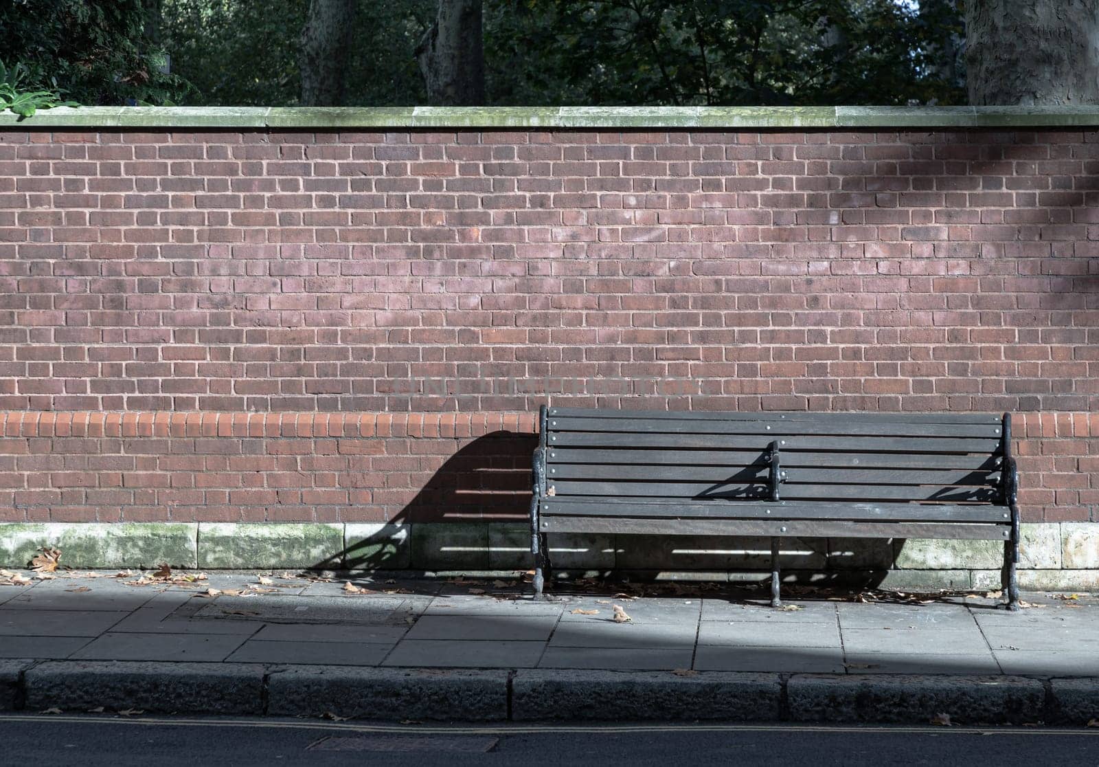One empty bench made of wooden boards and black iron stands on sidewalk in the street with bricks wall background. Wooden vintage bench on walkway, Bench on pedestrian footpath, Seat and unwind area, Space for text, Selective focus.