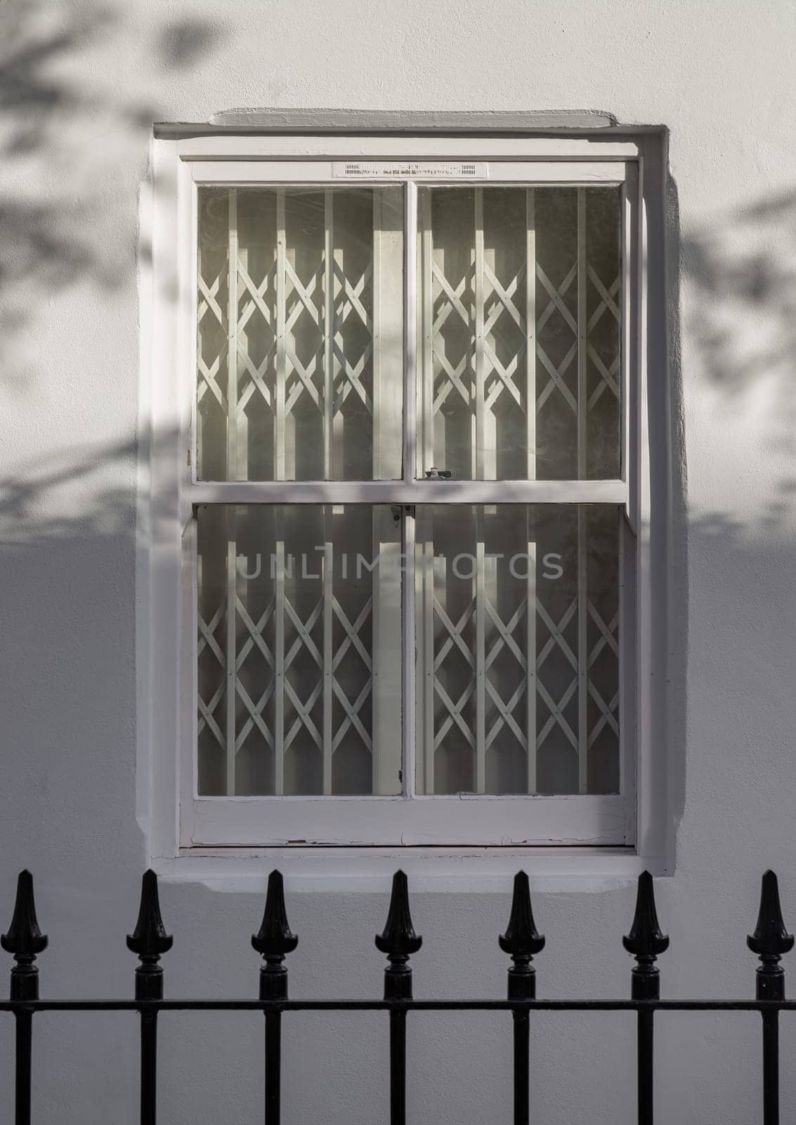 House exterior with wooden casement window on white wall with wrought iron fence. White steel folding gates in glass window, The sunshine lights through the glass window frame, Space for text, Selective focus.