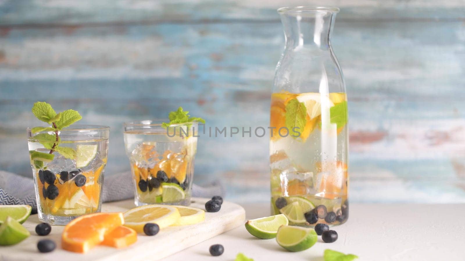Summer healthy cocktails of citrus infused waters, lemonades or mojitos, with lime lemon orange blueberries and mint, diet detox beverages, in glasses on light background.