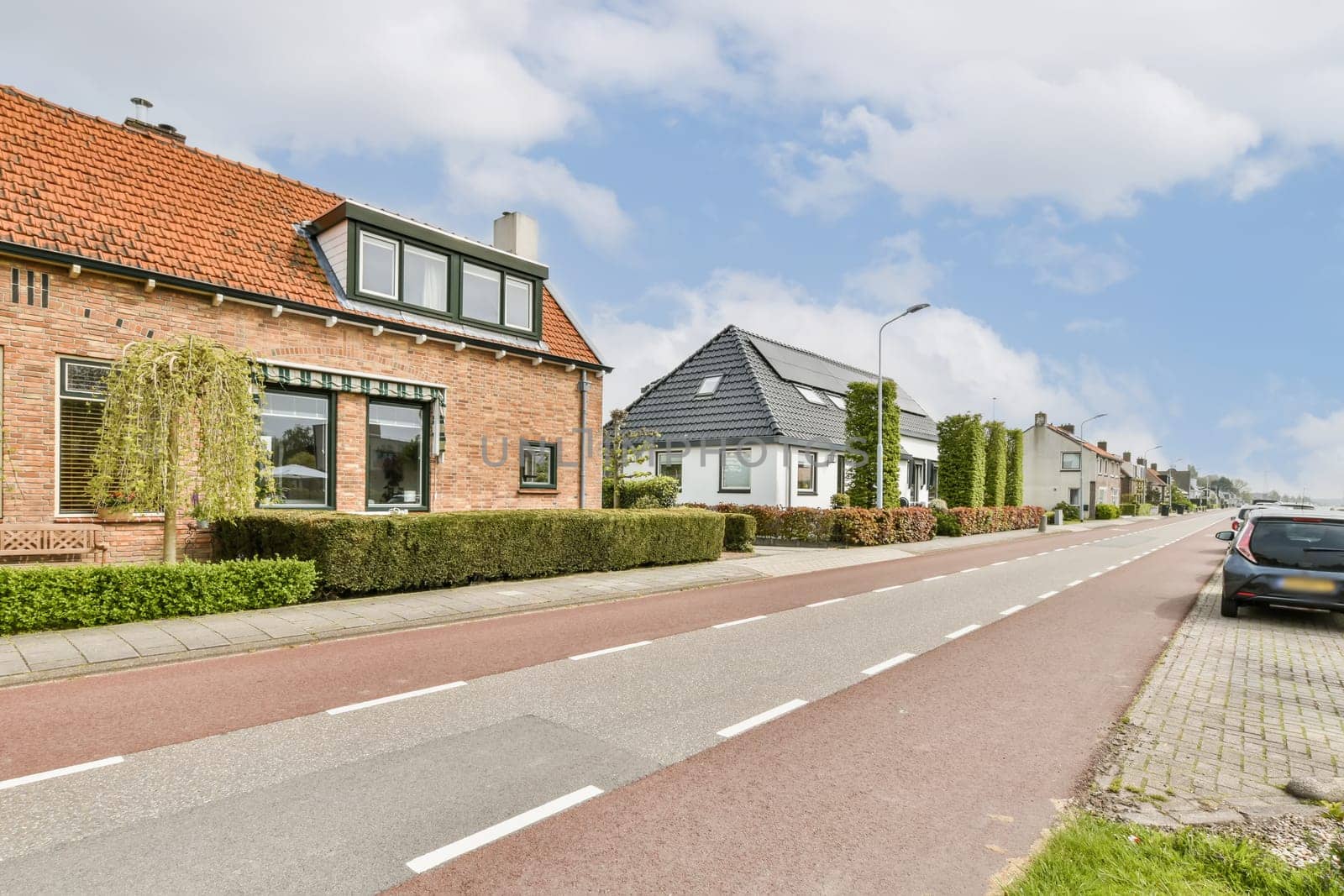 some houses on the side of a road with cars parked in front of them and one car driving down the street