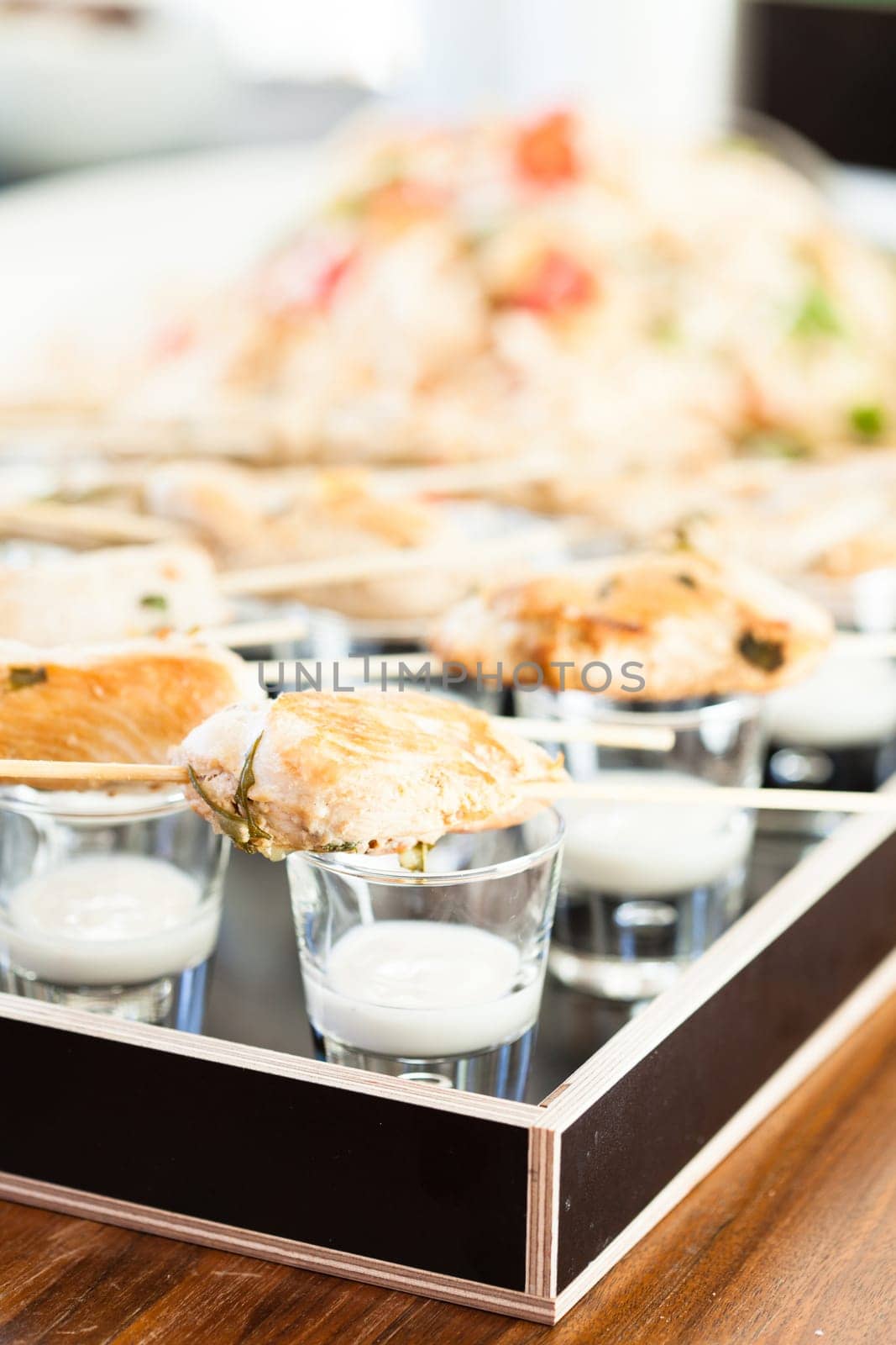 Closeup of pieces of cooked chicken on wooden skewers with mayonnaise based condiment in small glasses in serving tray
