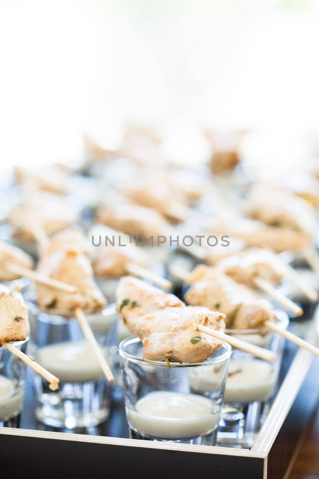 Closeup of pieces of cooked chicken on wooden skewers with mayonnaise based condiment in small glasses
