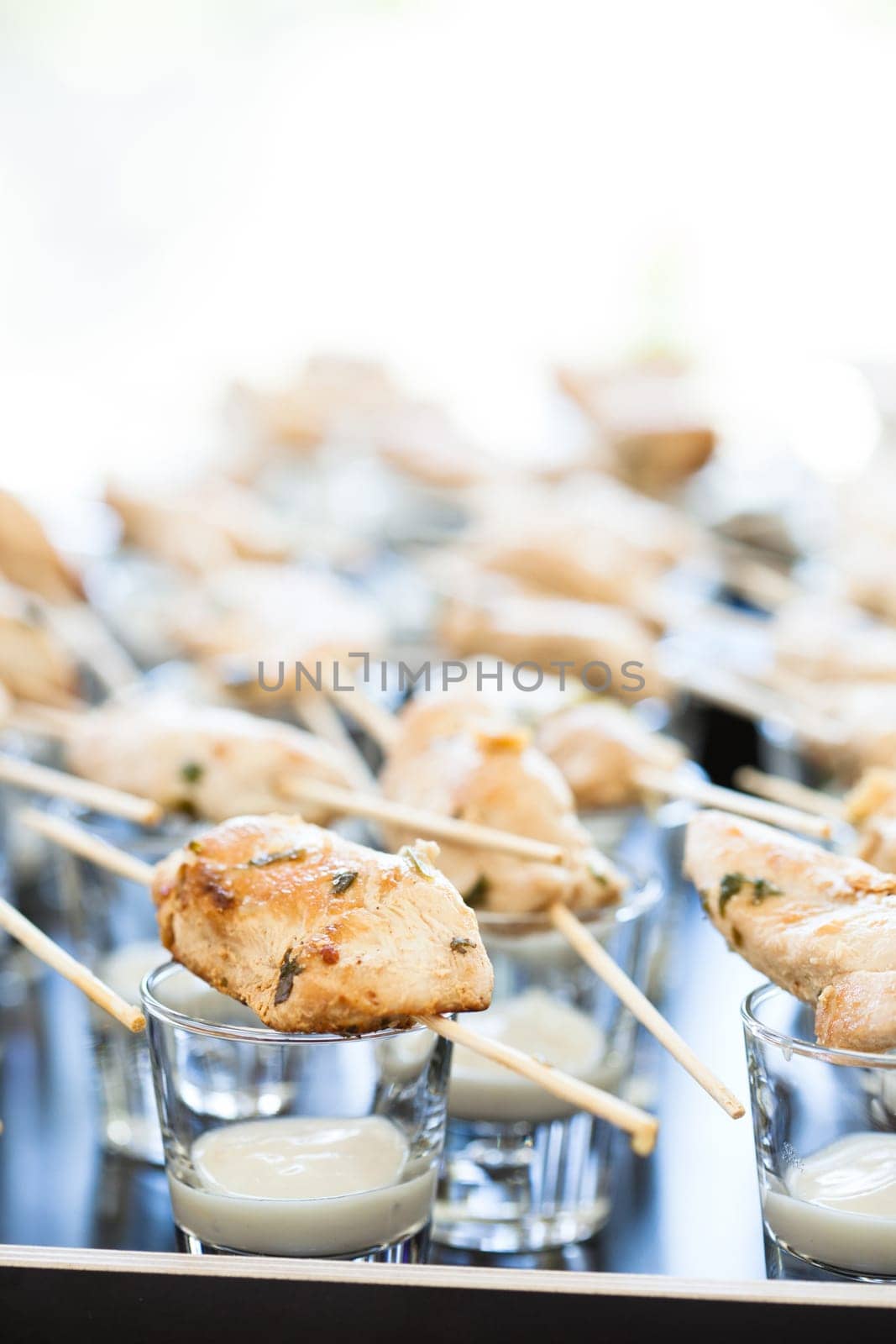 Closeup of pieces of cooked chicken on wooden skewers with mayonnaise based condiment in small glasses