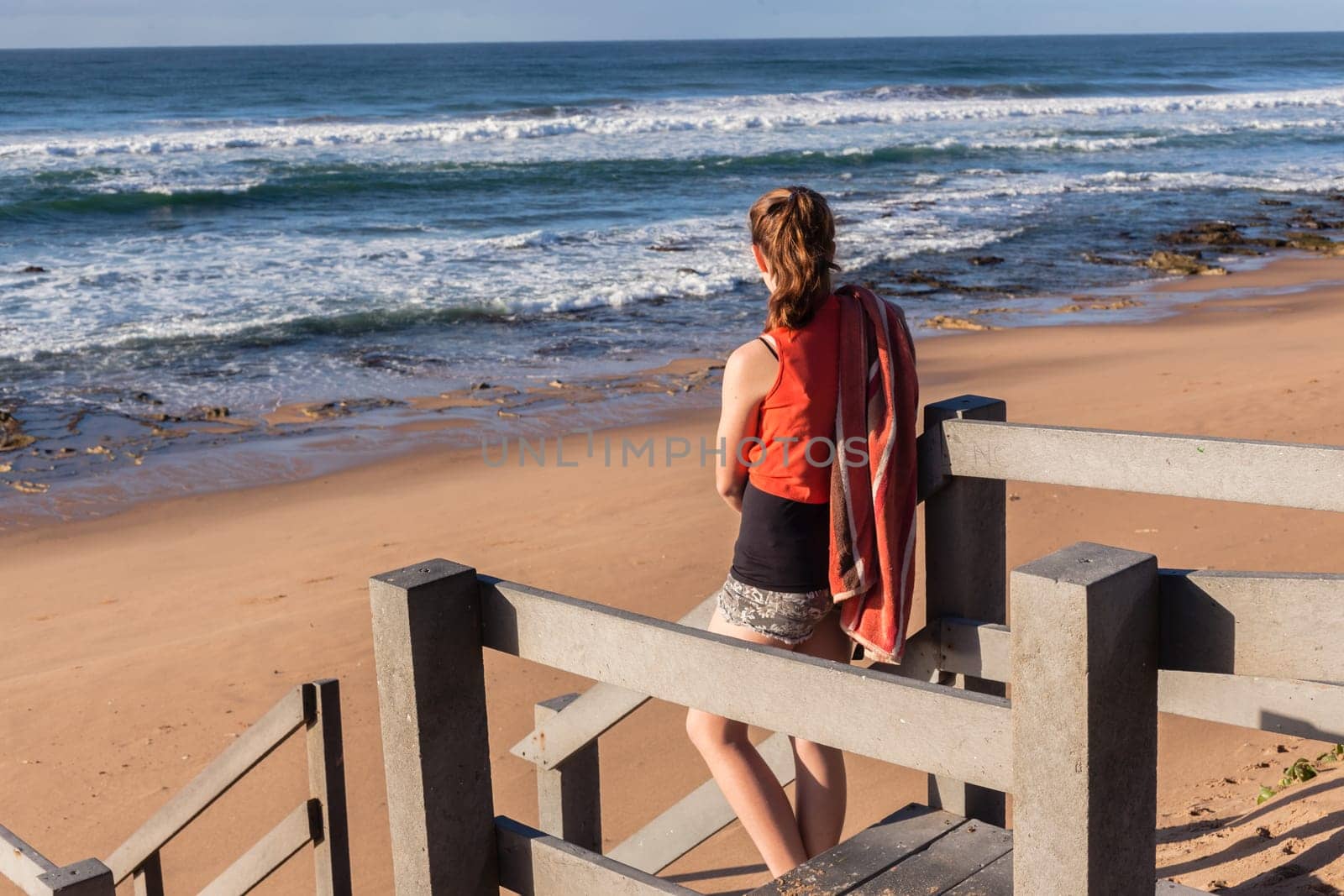 Girl teenager daughter overlooking landscape ocean beach sand rock reefs pools at low tide from stairs