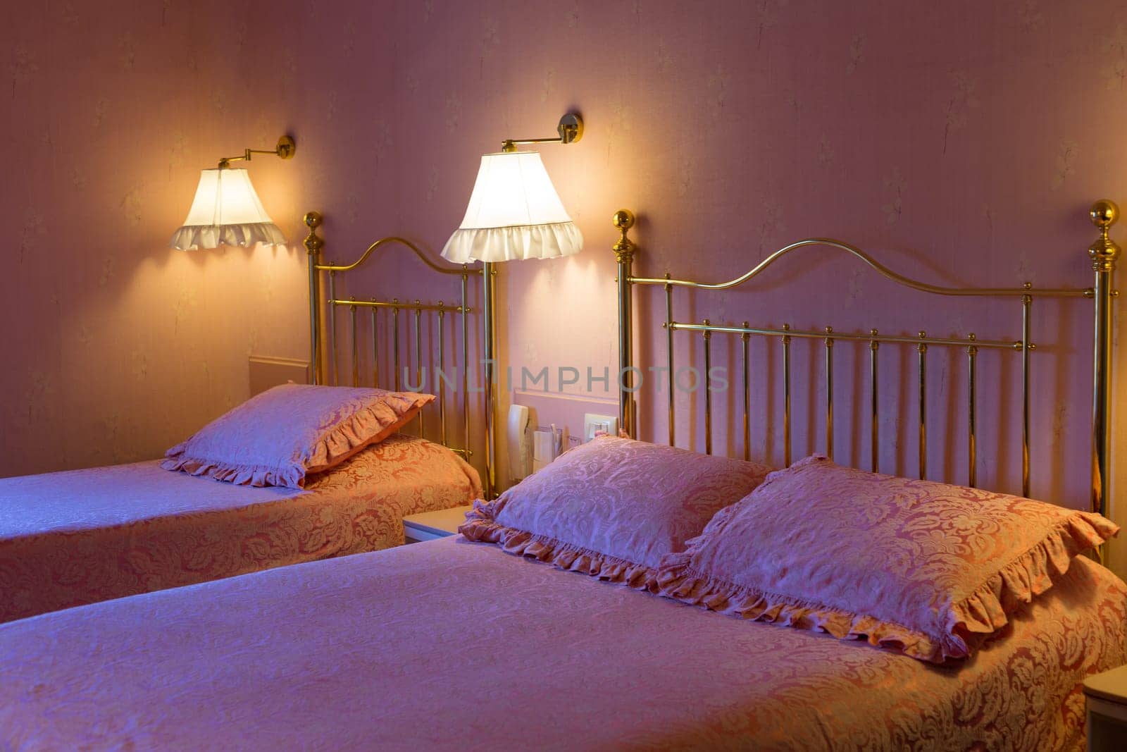 Trendy hotel in pink with two beds, in the light of the bedside lights and cold light from the window.