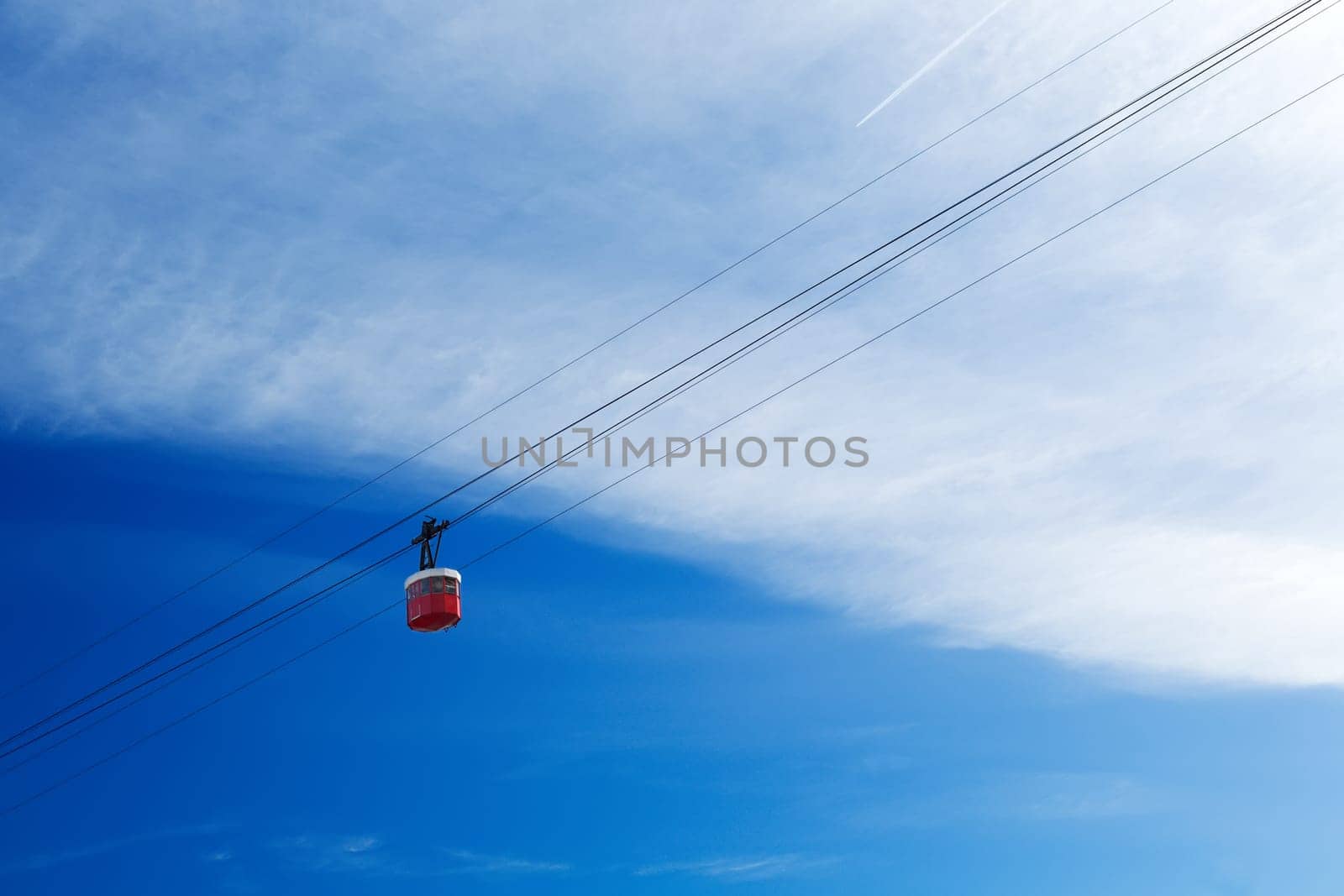 Red cable car cabin in the sky with clouds.
