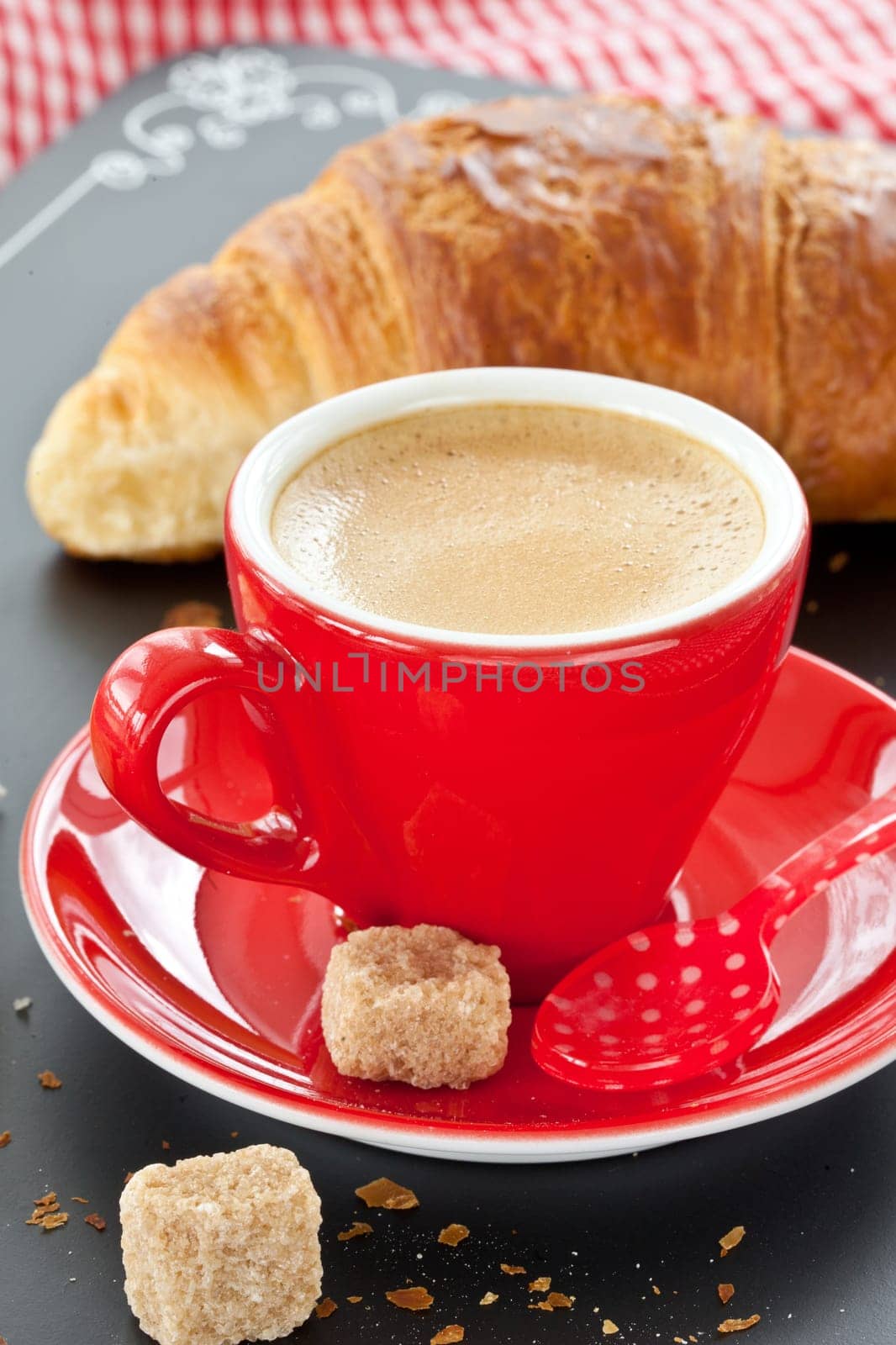 Red cup with coffee and a croissant on black
