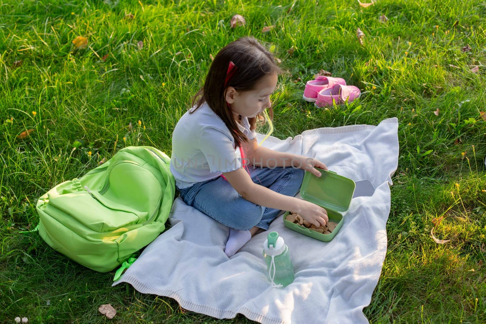Child enjoying picnic in park with healthy lunch and backpack on grass.