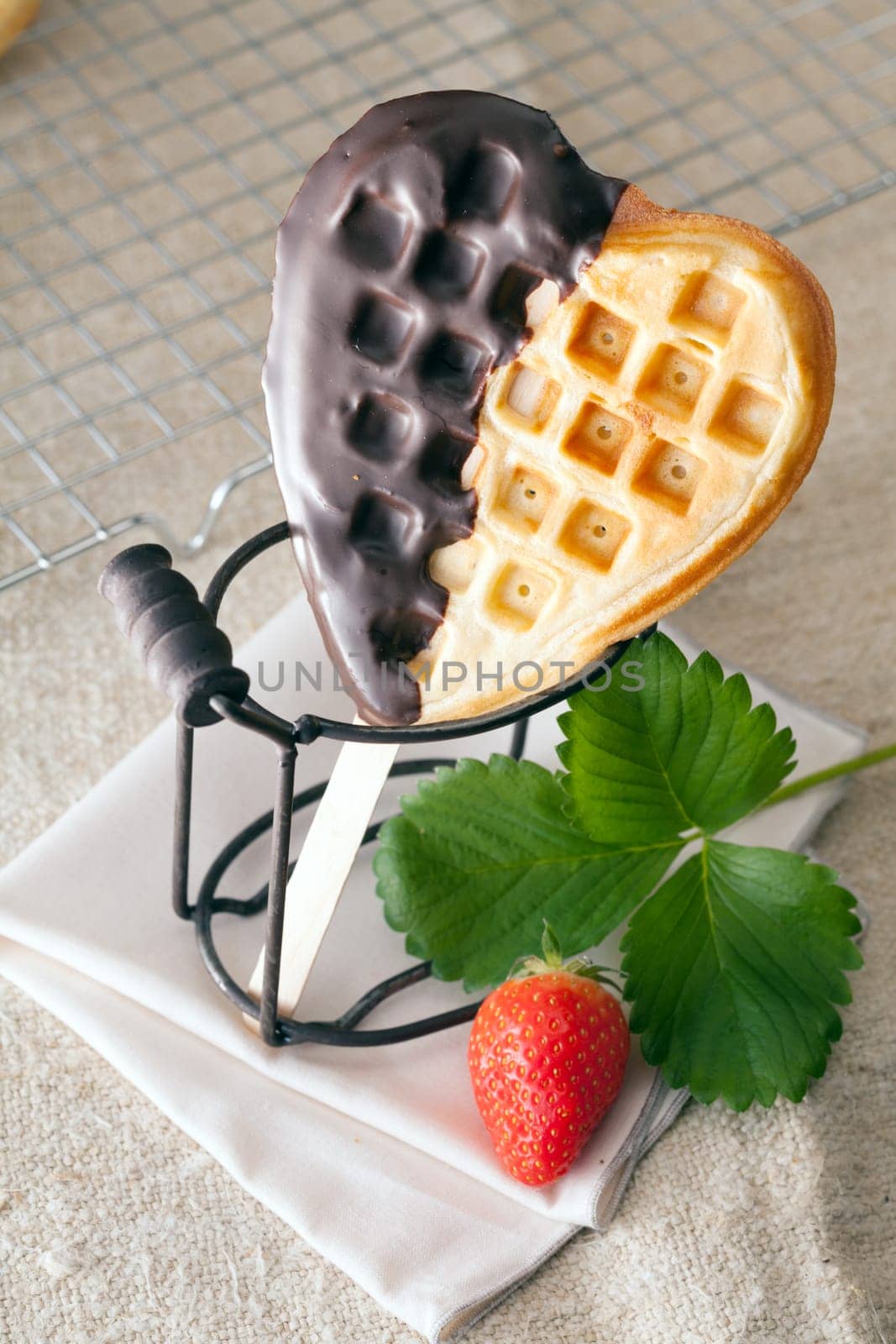 Crisp crunchy golden heart-shaped waffle coated on one side with chocolate presented with a ripe red strawberry and leaves for a gift to a loved one on Valentines or an anniversary