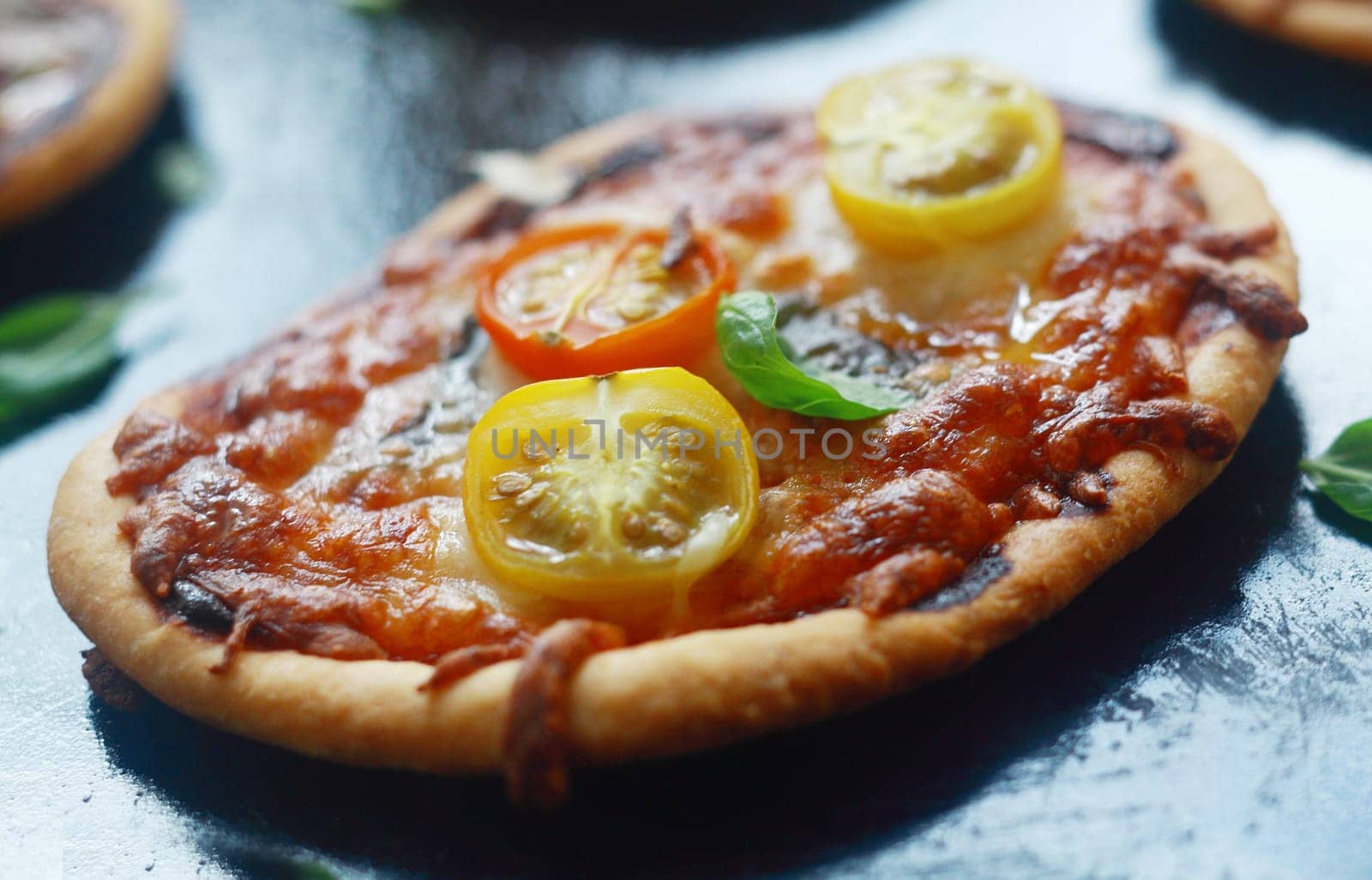 Italian mini pizza with cheese and tomato on a thick golden crusty base topped with fresh basil, close up view