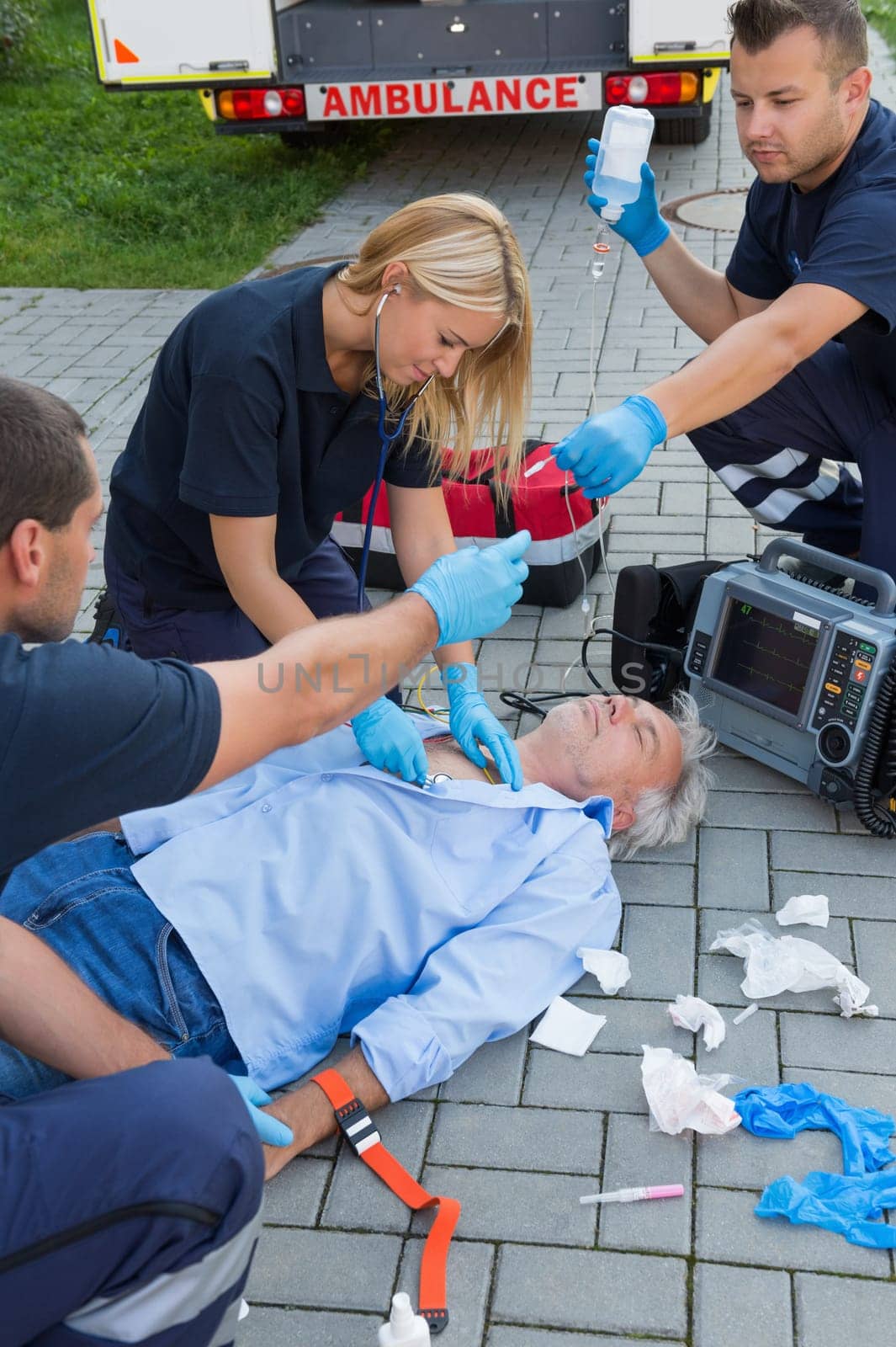 Paramedics examining unconscious senior man lying on ground