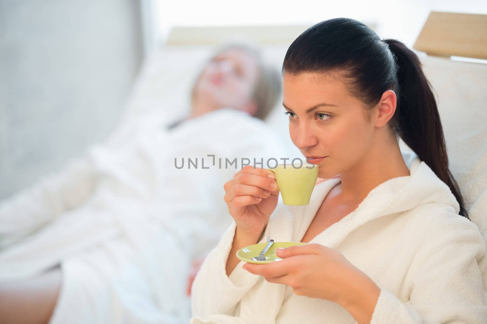 Woman drinking coffee at spa with friend in background