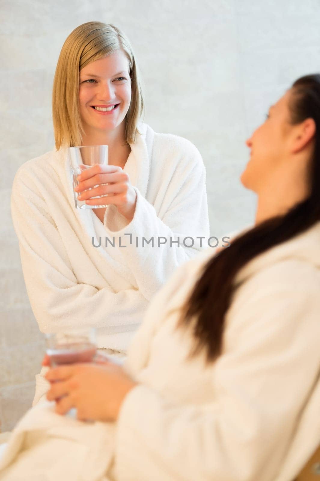 Smiling woman drinking water with friend at beauty spa