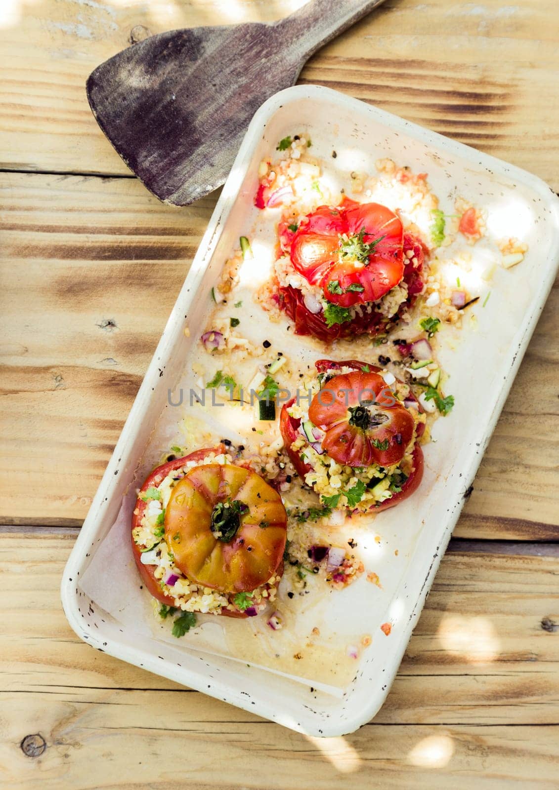 Overhead view of a plate of three ripe red baked tomatoes stuffed to overflowing with herbal grains for a healthy nutritious vegetarian meal