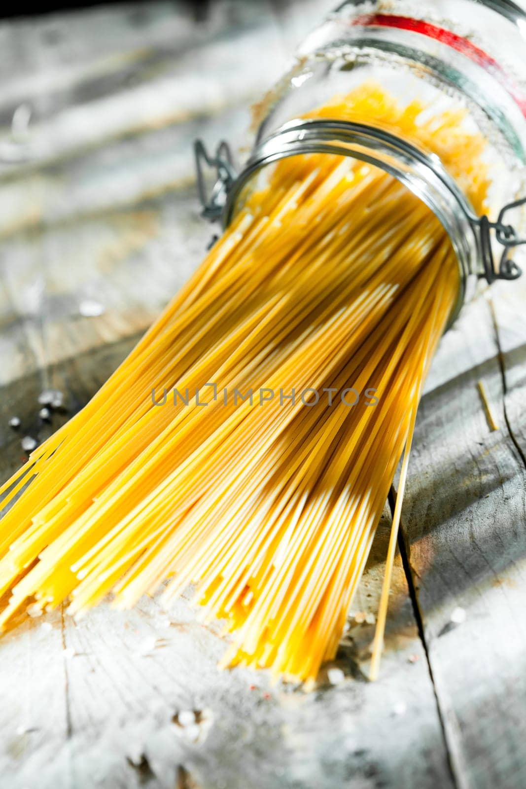 Glass jar of uncooked Italian spaghetti lying on its side in the sunshine on an old wooden rustic kitchen table