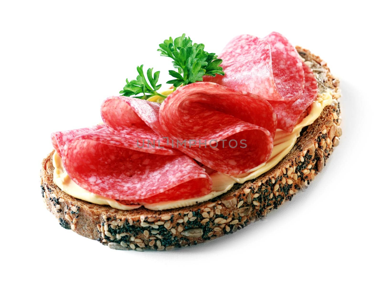 Tasty appetizer of thinly sliced spicy salami on wholewheat bread with a seed crust and liberal spread of butter or margarine topped with parsley, on white