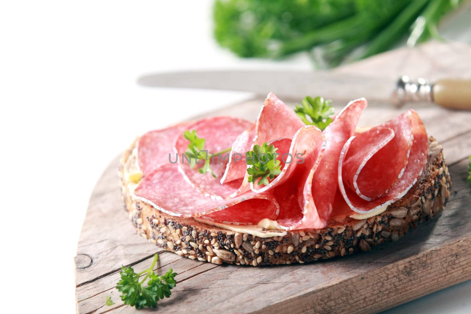 Thinly sliced tasty spicy Italian salami sausage on wholegrain bread with seeds served on a rustic wooden board garnished with fresh chopped parsley