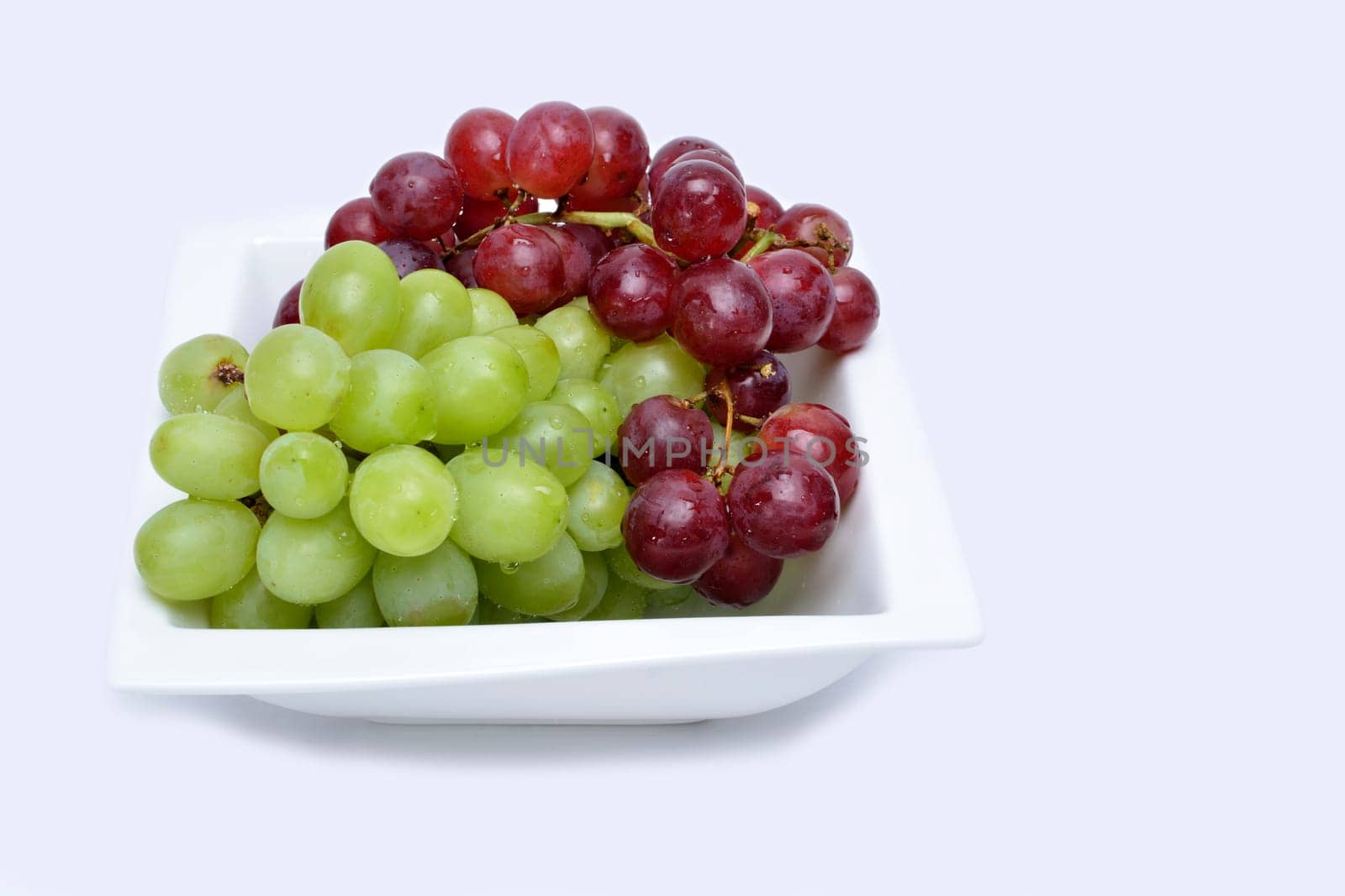 Bunch of red and green grapes on a white ceramic saucer
