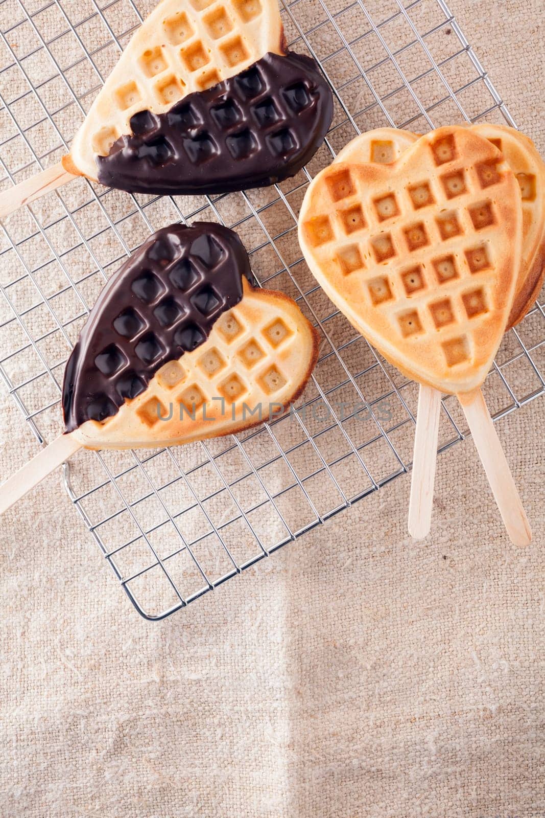Romantic heart shaped waffle lollipops with a crisp golden wafer dipped on one side in dark chocolate cooling on a wire tray in a kitchen for Valentines or an anniversary