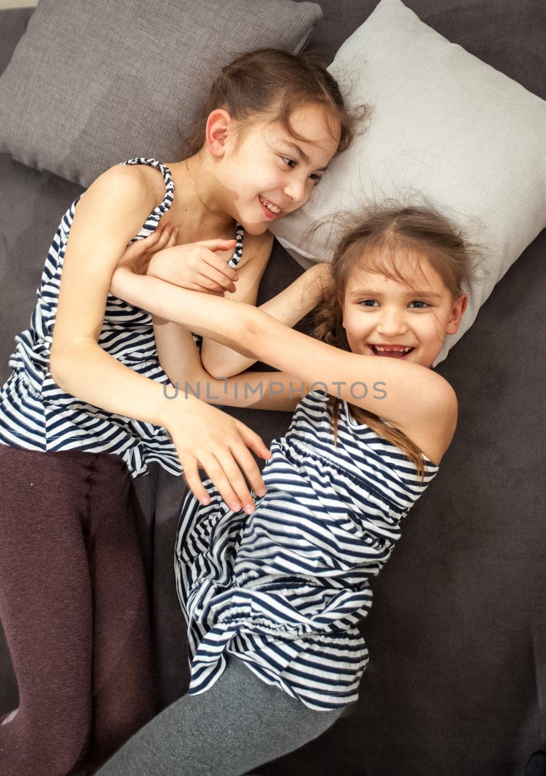 Portrait of two young sisters pushing each other on bed
