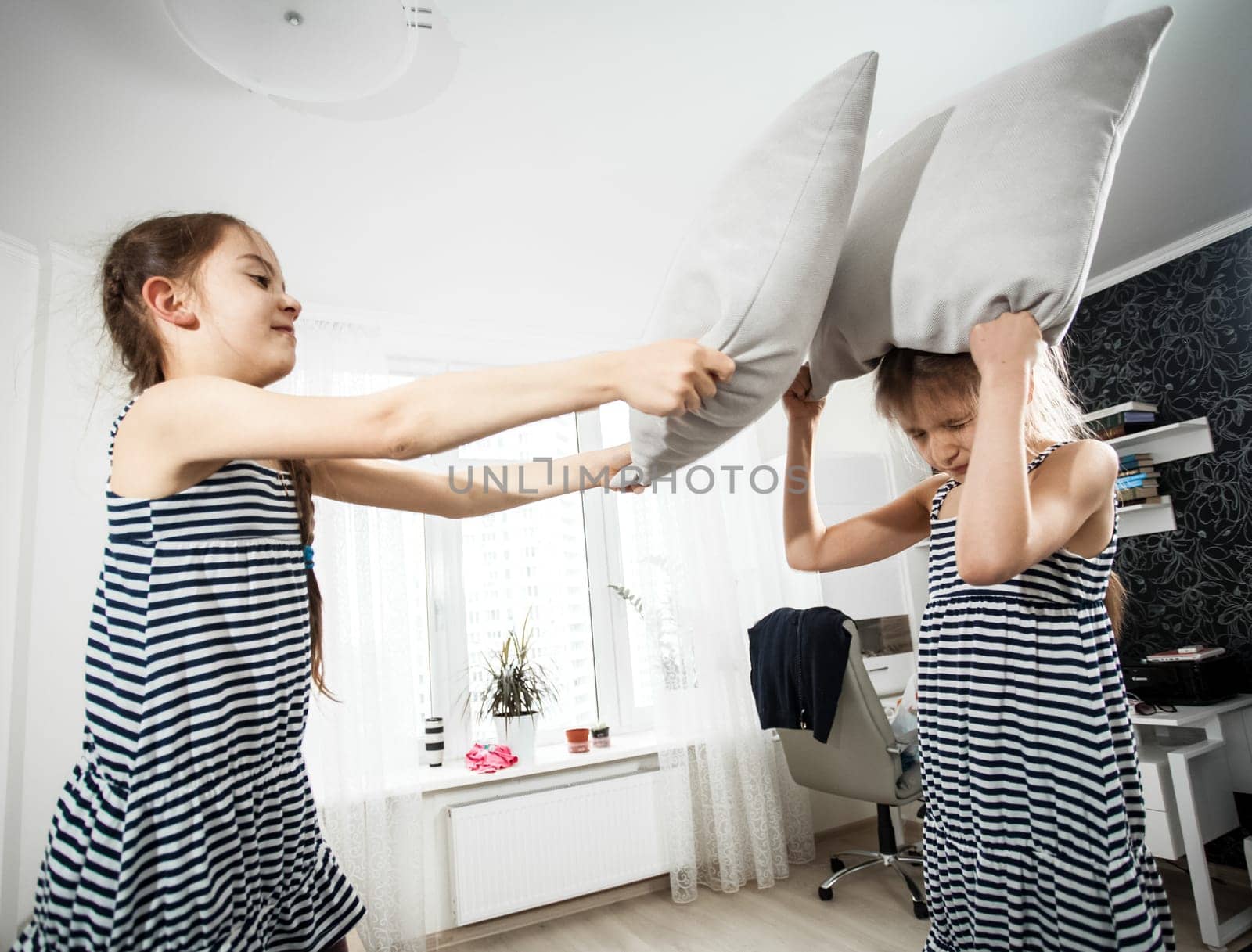 Closeup portrait of girl hitting sister with pillow during fight