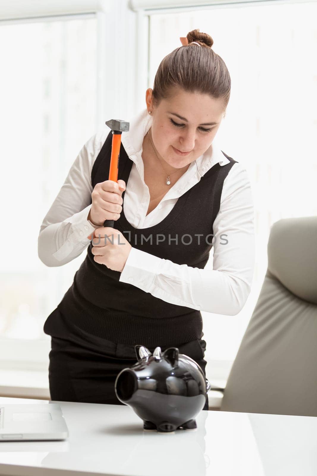 Closeup portrait of brunette businesswoman trying to break piggy bank