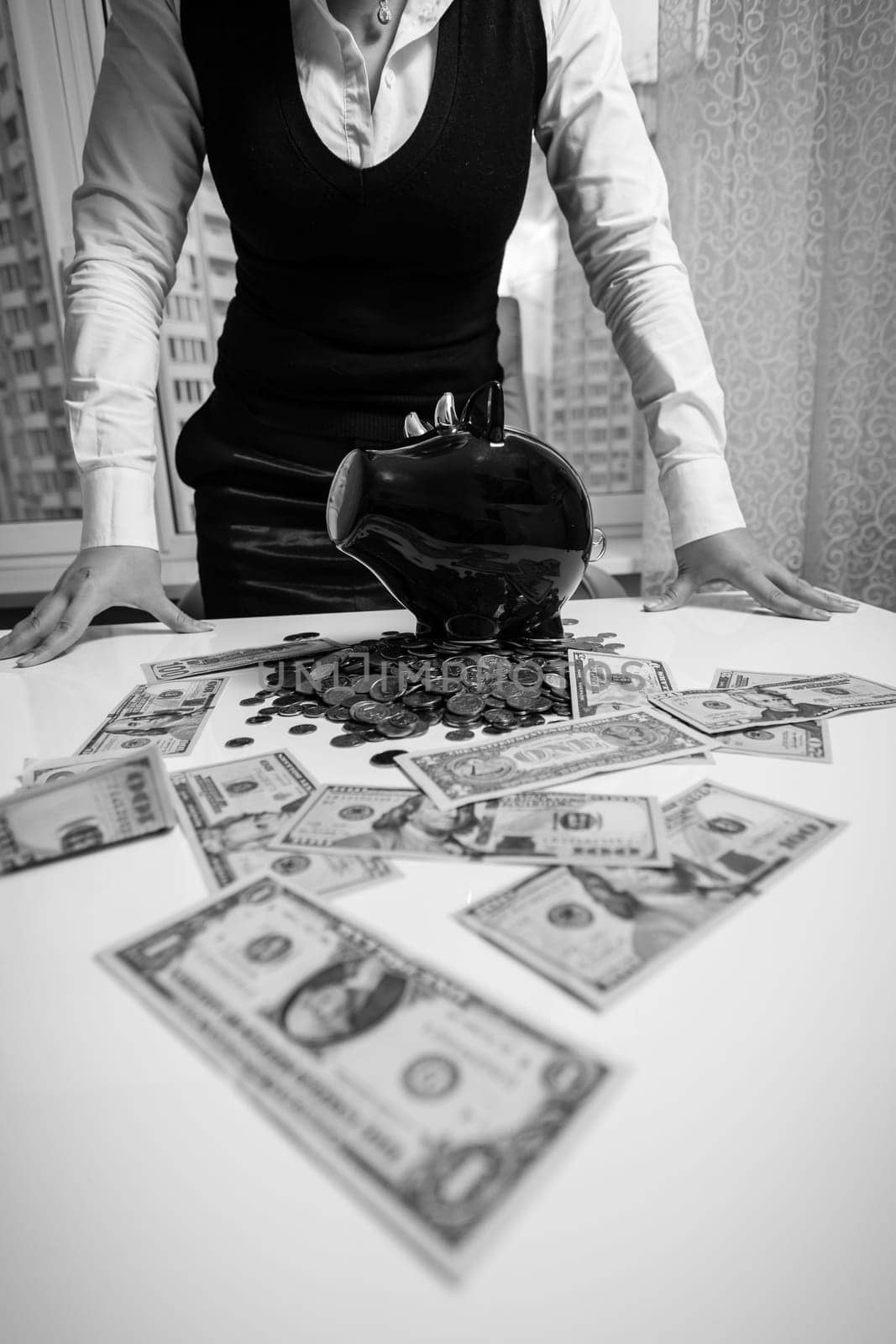 Black and white photo of woman standing behind table with banknotes and piggy bank
