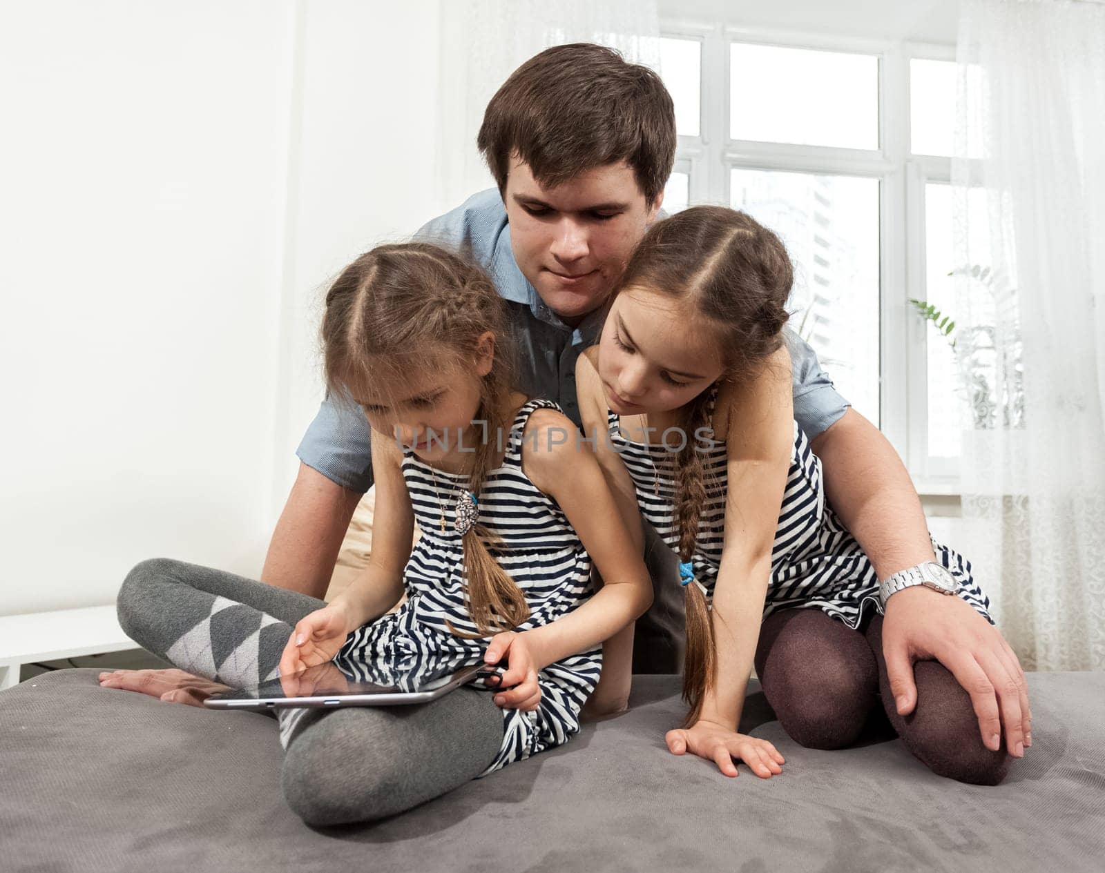 Portrait of man hugging two young girls looking at tablet