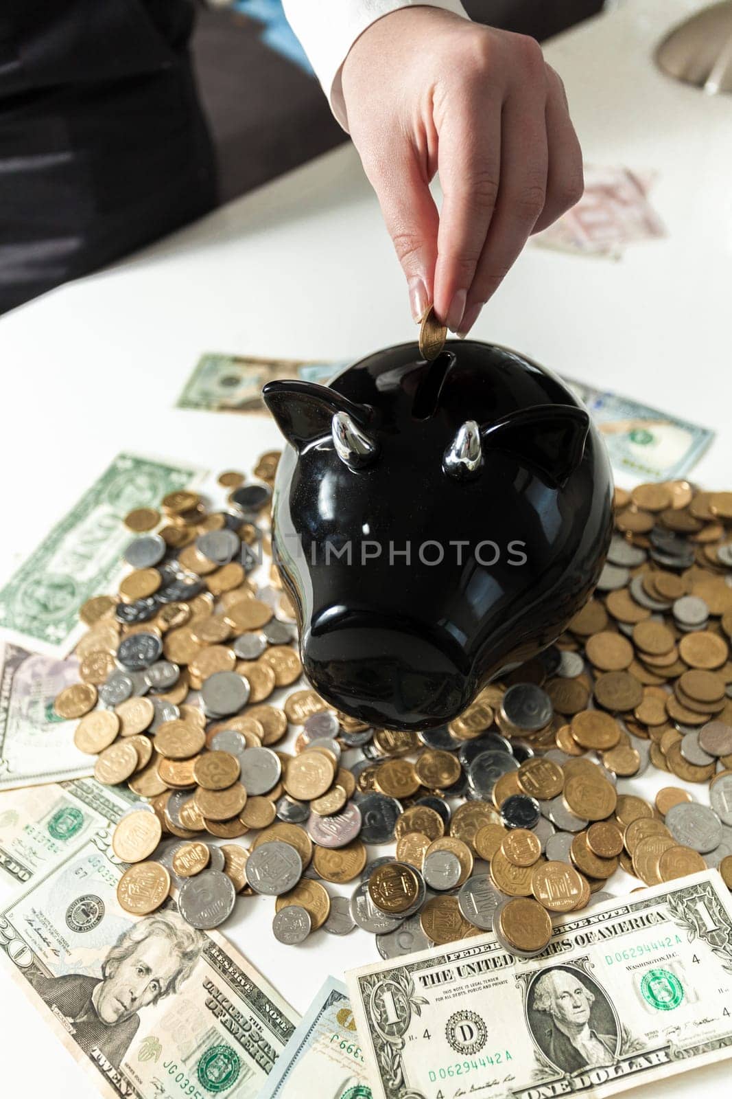 Closeup photo of hand putting coin in black piggy bank