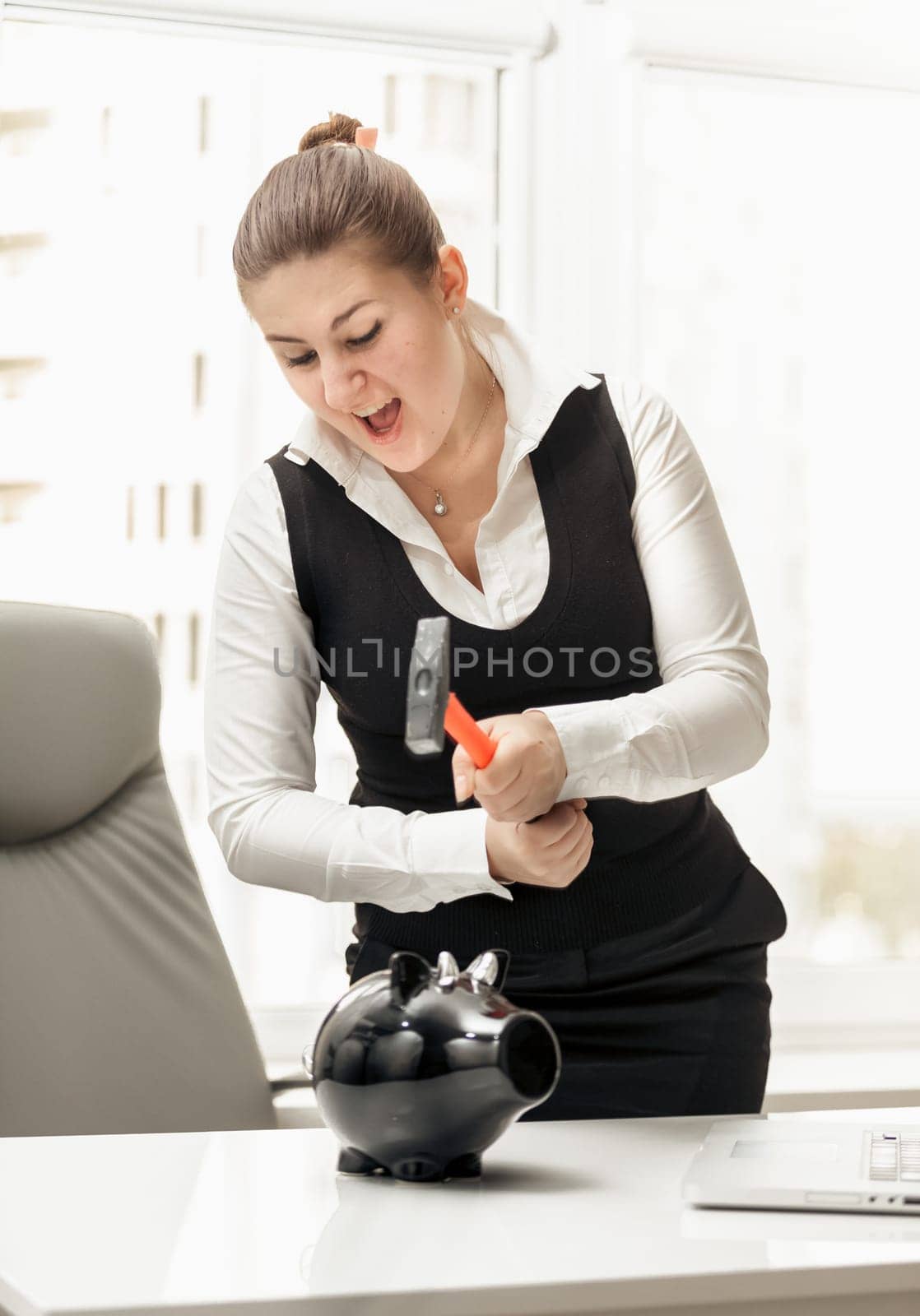 Portrait of angry businesswoman breaking piggy bank with hammer
