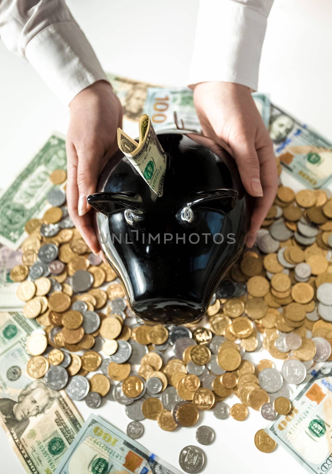 Closeup photo of woman holding black pig moneybox on pile of coins